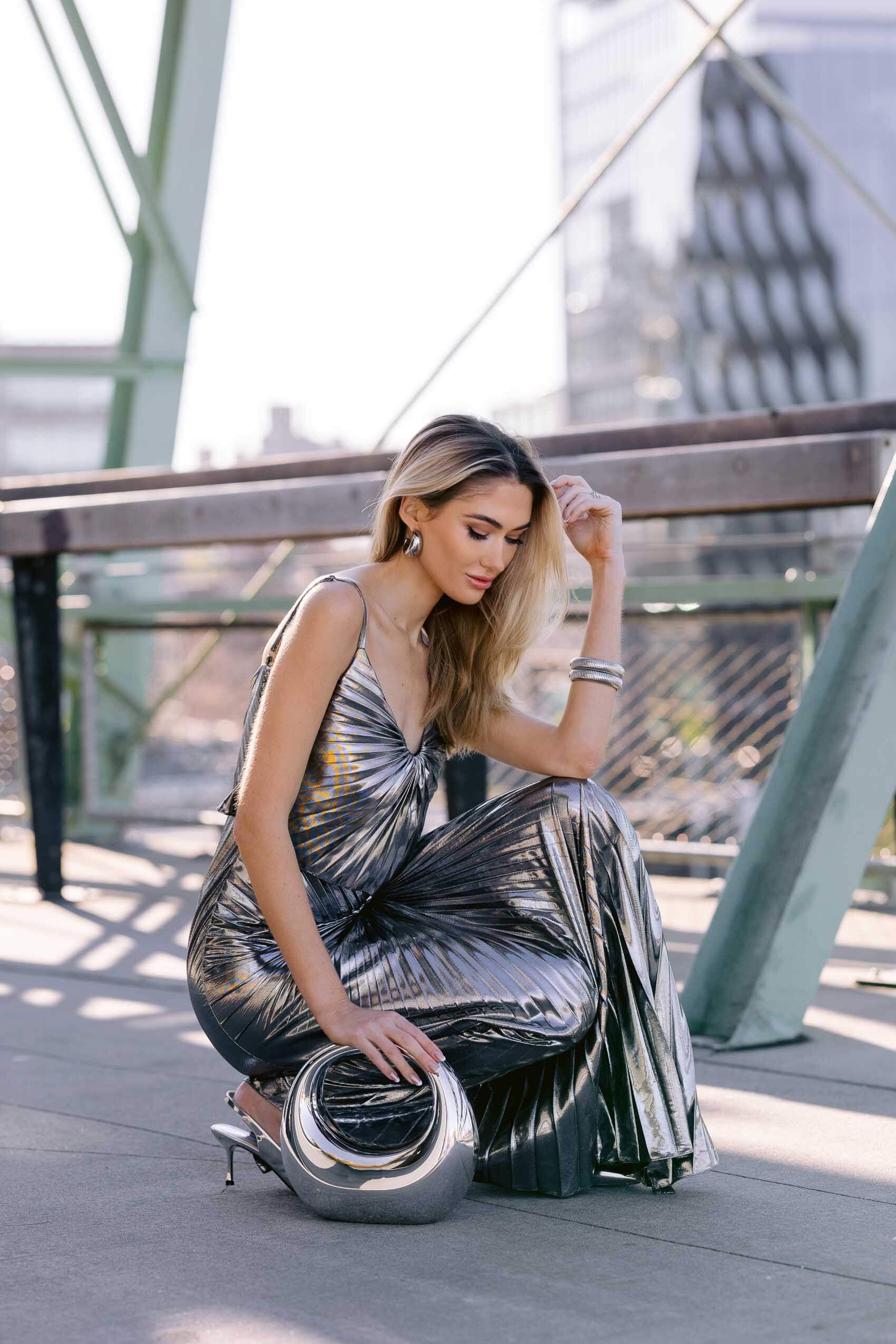 A woman in the Georgia Hardinge Dazed Dress, posing with a metallic bag and silver accessories